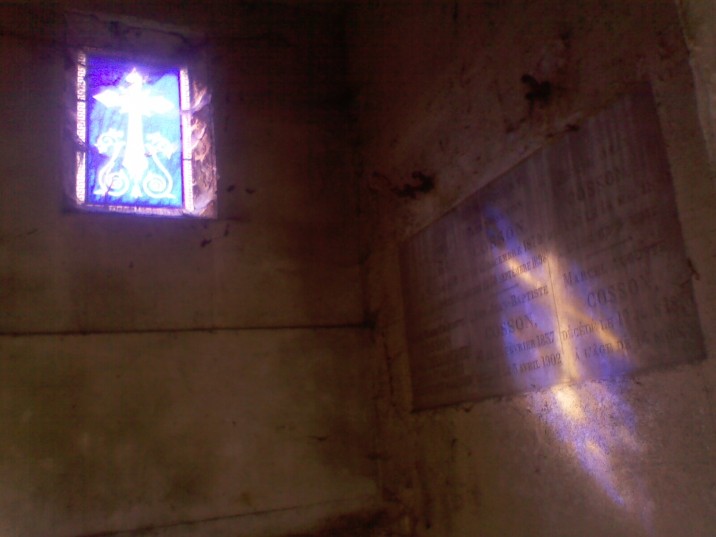 Sunlight shines through a blue stained-glass window, projecting an orange cross on a blue background below on the right-hand wall