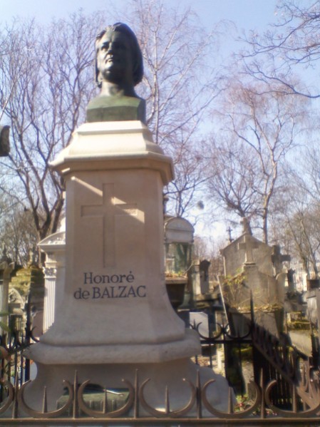 A tapering white monument with the name 'Honoré de BALZAC' at the base in black letters. A green bust is mounted on top