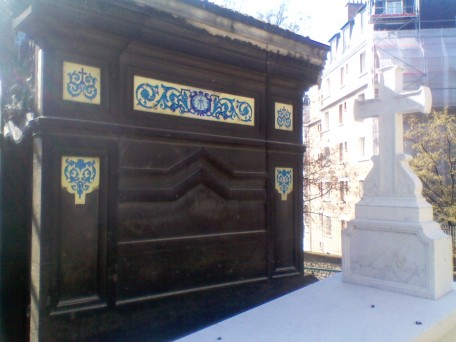 Bright blue and yellow panels on a black rectangular monument. A very pale white monument with a cross is to the right