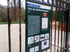 A green sign mounted on a fence with peeling green paint, explaining the regulations and history of the park