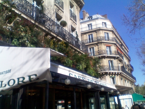View of the Café de Flore. The café's name is prominently displayed on two white banners above the establishment itself; mounted on the building above are numerous leafy plants